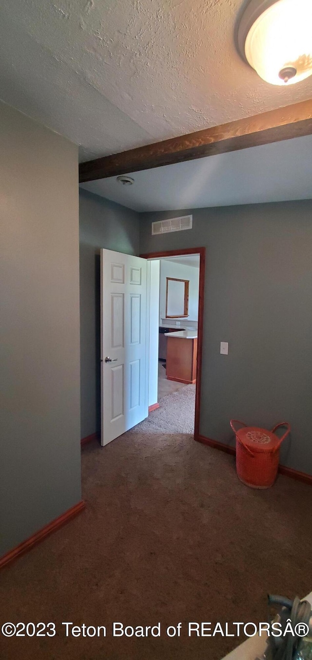 spare room featuring dark carpet, a textured ceiling, and beamed ceiling