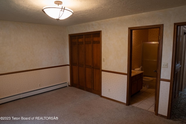 unfurnished bedroom with light colored carpet, ensuite bath, a baseboard heating unit, a textured ceiling, and a closet