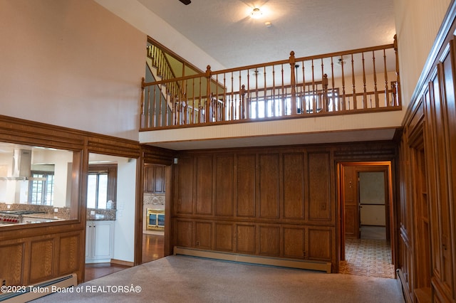 interior space with baseboard heating, dark carpet, and a high ceiling