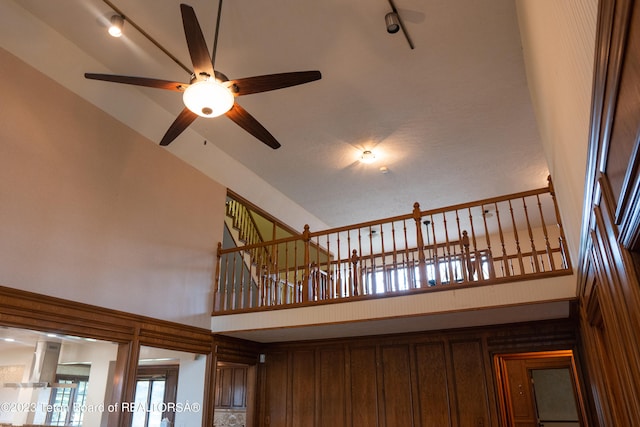 stairway with ceiling fan, high vaulted ceiling, and rail lighting