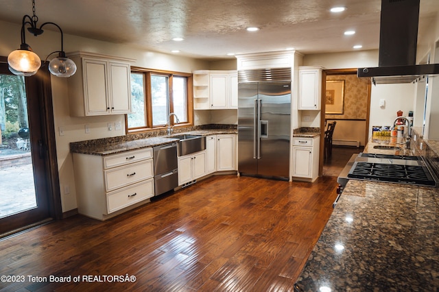 kitchen with dark stone counters, appliances with stainless steel finishes, island exhaust hood, dark hardwood / wood-style floors, and sink