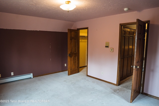 unfurnished bedroom with a closet, a textured ceiling, light colored carpet, a baseboard heating unit, and a spacious closet