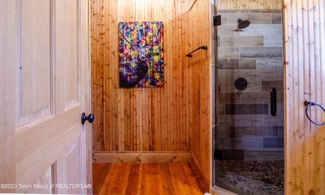 bathroom featuring a shower with door, wood walls, and wood-type flooring