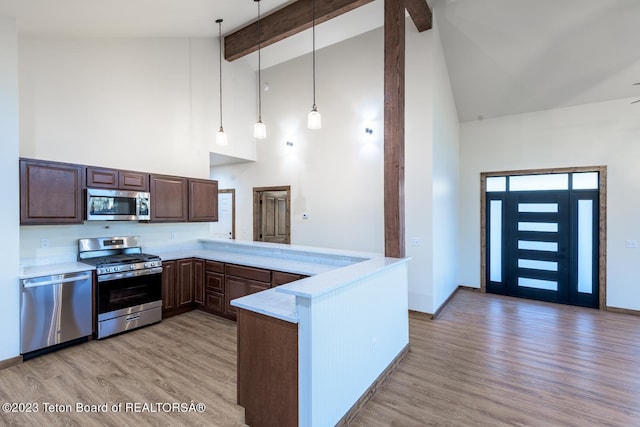 kitchen featuring decorative light fixtures, light hardwood / wood-style flooring, stainless steel appliances, kitchen peninsula, and high vaulted ceiling