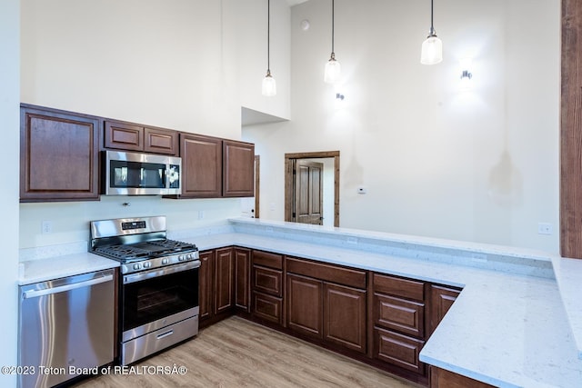 kitchen with light wood-type flooring, stainless steel appliances, kitchen peninsula, hanging light fixtures, and a towering ceiling