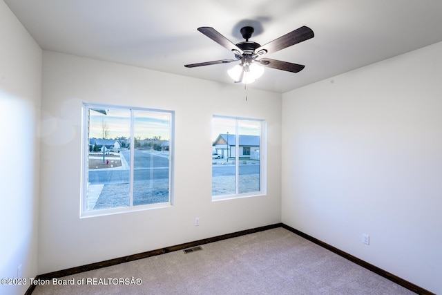 carpeted spare room featuring ceiling fan and plenty of natural light