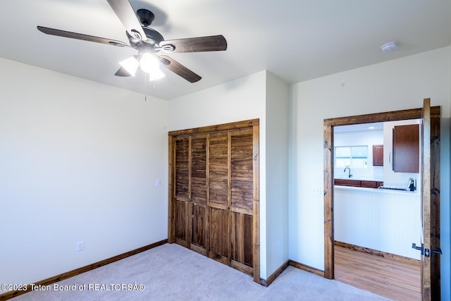 unfurnished bedroom with a closet, ceiling fan, sink, and light carpet