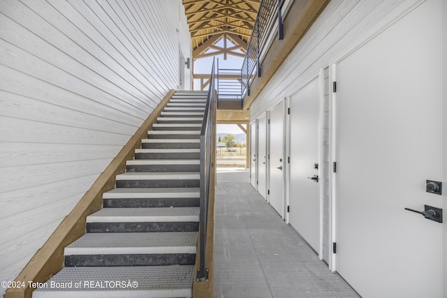 staircase featuring high vaulted ceiling, wood walls, and tile patterned floors