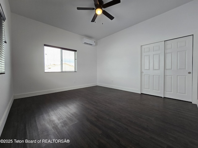 unfurnished bedroom with an AC wall unit, dark wood finished floors, and baseboards