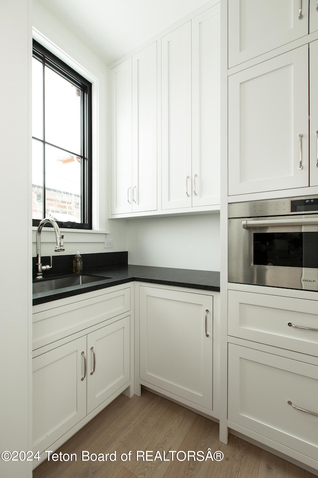 kitchen with sink, stainless steel oven, light wood-type flooring, and white cabinetry