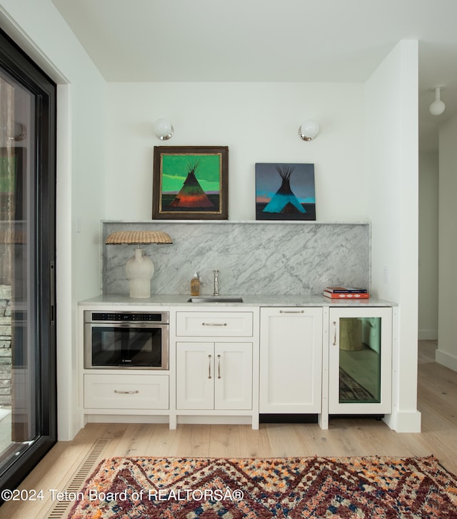 bar with beverage cooler, oven, sink, white cabinets, and light wood-type flooring