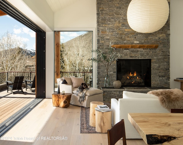 living room featuring a stone fireplace, vaulted ceiling, and hardwood / wood-style flooring