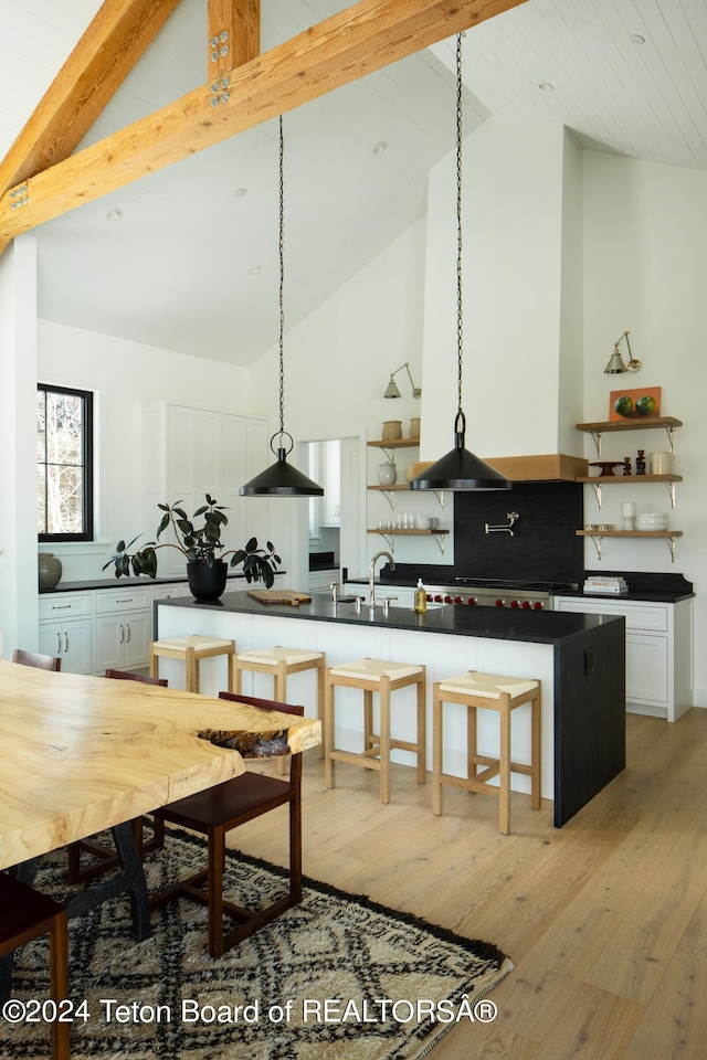 kitchen featuring high vaulted ceiling, decorative light fixtures, white cabinetry, and light wood-type flooring