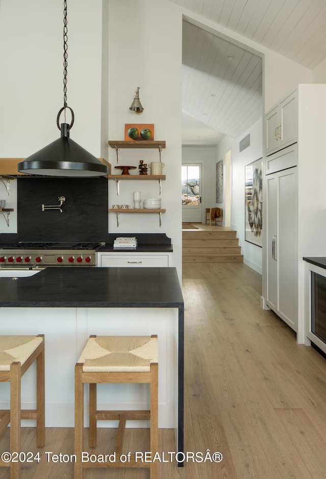 kitchen featuring lofted ceiling, light hardwood / wood-style floors, backsplash, and a kitchen breakfast bar