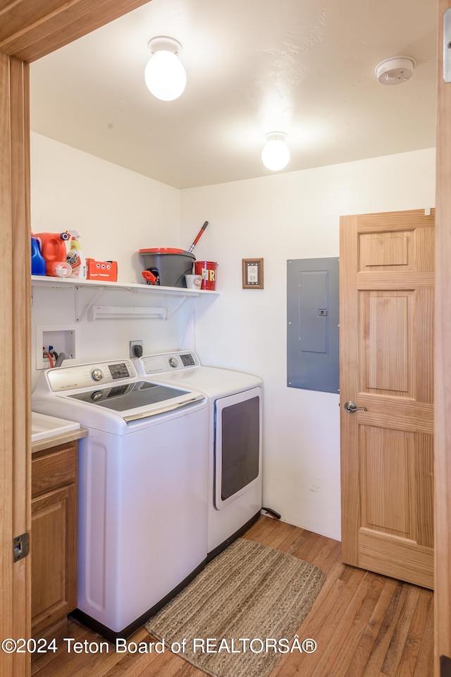 washroom with cabinets, electric panel, washer and dryer, and light wood-type flooring