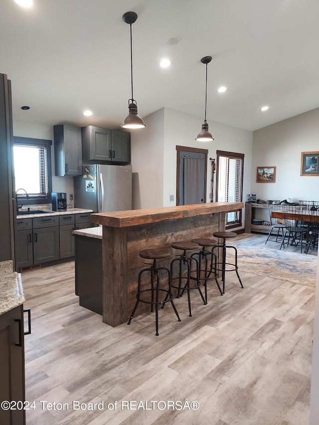 kitchen with a breakfast bar, refrigerator, a wealth of natural light, and light hardwood / wood-style flooring