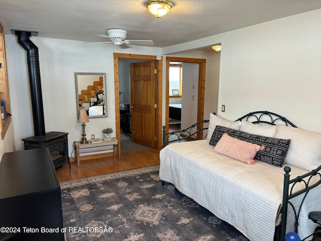 bedroom featuring dark hardwood / wood-style floors, a textured ceiling, ceiling fan, and a wood stove