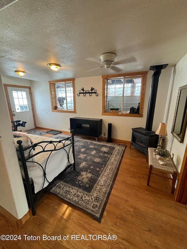 bedroom featuring a textured ceiling, ceiling fan, a wood stove, and wood-type flooring