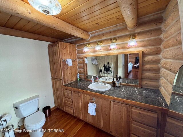 bathroom with log walls, oversized vanity, hardwood / wood-style flooring, toilet, and beam ceiling