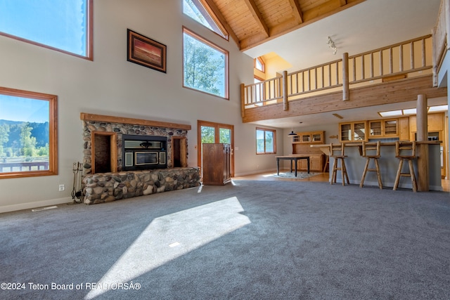 living room featuring a stone fireplace, beam ceiling, carpet flooring, wood ceiling, and high vaulted ceiling