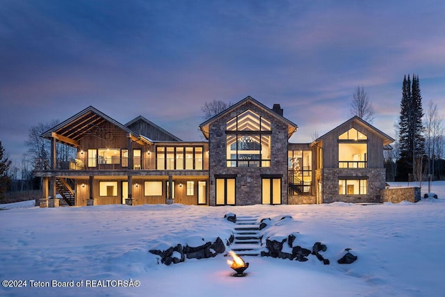 snow covered property with stone siding, stairway, a chimney, and board and batten siding