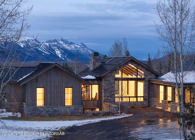 view of front of property featuring metal roof, a mountain view, stone siding, driveway, and a chimney