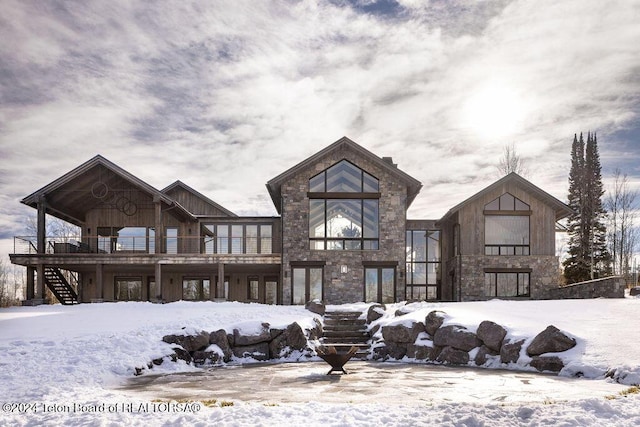 snow covered back of property with stone siding and stairway