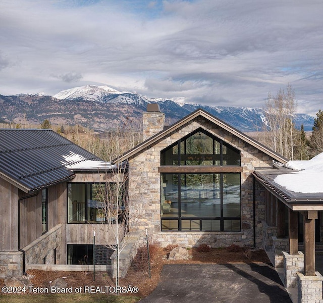 exterior space featuring metal roof, a chimney, stone siding, and a mountain view