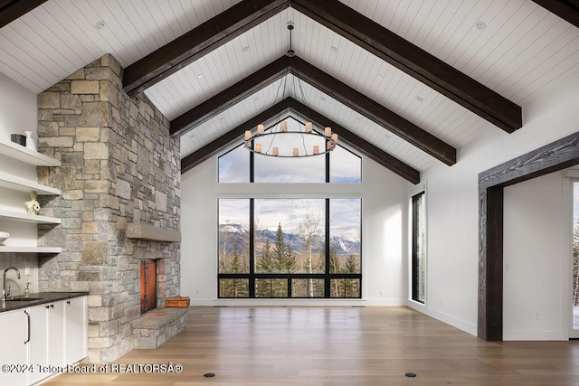 unfurnished living room featuring wood finished floors, beam ceiling, a stone fireplace, high vaulted ceiling, and a sink