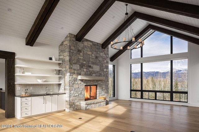 unfurnished living room with beamed ceiling, wood finished floors, an inviting chandelier, a stone fireplace, and high vaulted ceiling