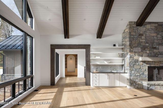 unfurnished living room featuring baseboards, visible vents, beamed ceiling, light wood-style floors, and a fireplace