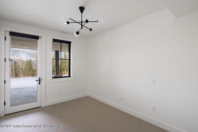 carpeted empty room featuring a notable chandelier, visible vents, and baseboards