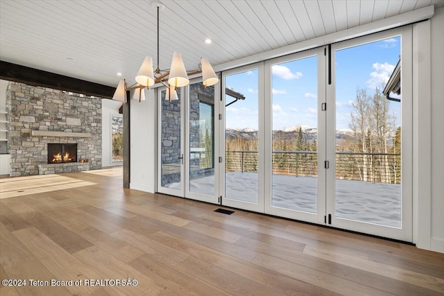 entryway featuring a stone fireplace, beamed ceiling, wood finished floors, and a healthy amount of sunlight