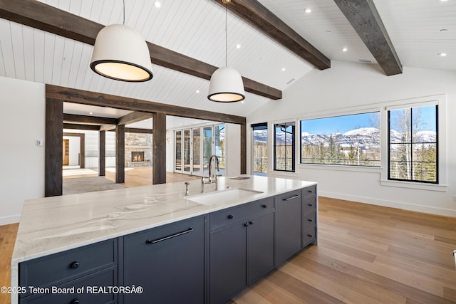 kitchen featuring light stone counters, a sink, lofted ceiling with beams, and light wood finished floors