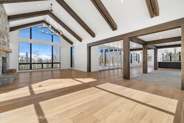 unfurnished living room with a healthy amount of sunlight, wood-type flooring, high vaulted ceiling, and a stone fireplace