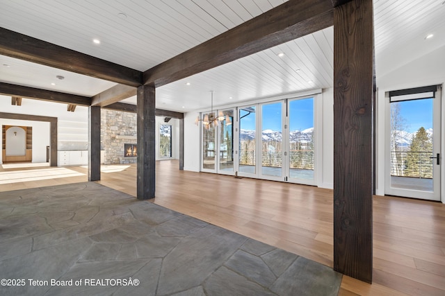 unfurnished living room with a healthy amount of sunlight, a fireplace, beamed ceiling, and wood finished floors