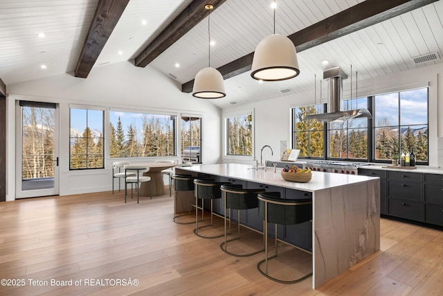 kitchen with a kitchen island with sink, light countertops, lofted ceiling with beams, and visible vents