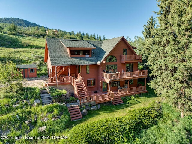 back of property with a yard, an outdoor structure, roof with shingles, a balcony, and stairs
