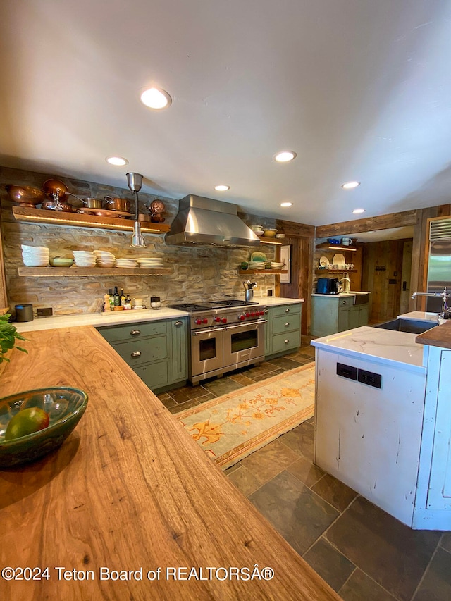 kitchen featuring range with two ovens, green cabinets, dark tile flooring, wall chimney range hood, and sink