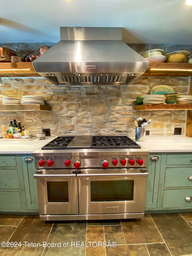 kitchen featuring range with two ovens, green cabinetry, tasteful backsplash, wall chimney range hood, and dark tile floors