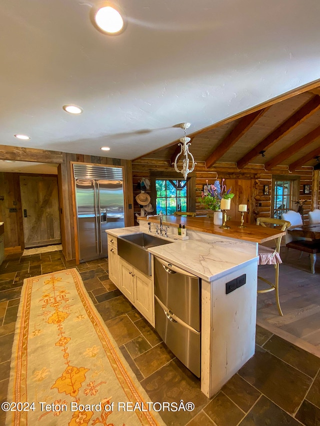 kitchen with light stone countertops, rustic walls, appliances with stainless steel finishes, sink, and an island with sink