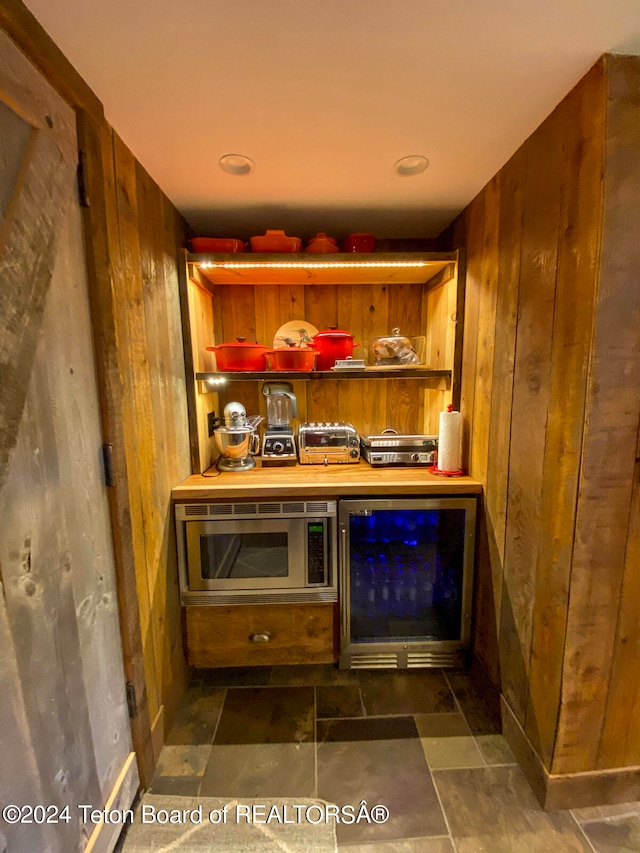 bar featuring dark tile floors, wine cooler, stainless steel microwave, and wooden walls