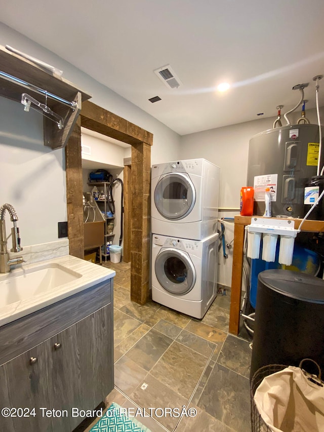 laundry room with water heater, dark tile flooring, stacked washer / dryer, and sink