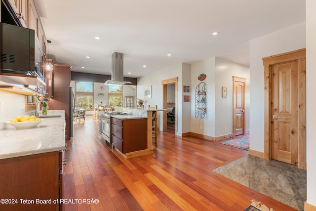 kitchen featuring dark hardwood / wood-style floors, island range hood, appliances with stainless steel finishes, light stone countertops, and a spacious island