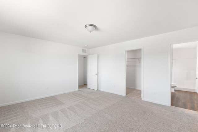 unfurnished bedroom with a spacious closet, a closet, connected bathroom, and light colored carpet