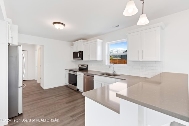 kitchen featuring stainless steel appliances, hanging light fixtures, hardwood / wood-style floors, white cabinets, and kitchen peninsula