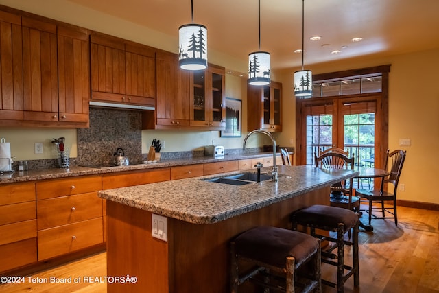 kitchen featuring decorative backsplash, sink, a kitchen island with sink, light hardwood / wood-style floors, and a breakfast bar