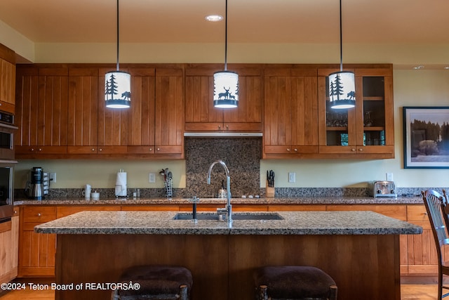 kitchen featuring dark stone countertops, a breakfast bar, an island with sink, hanging light fixtures, and sink