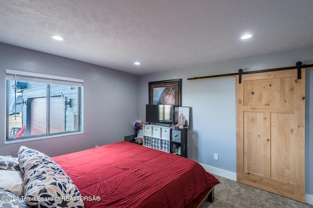 carpeted bedroom featuring a barn door and a textured ceiling