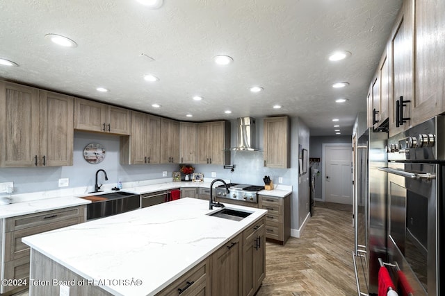 kitchen featuring wall chimney range hood, sink, an island with sink, and appliances with stainless steel finishes